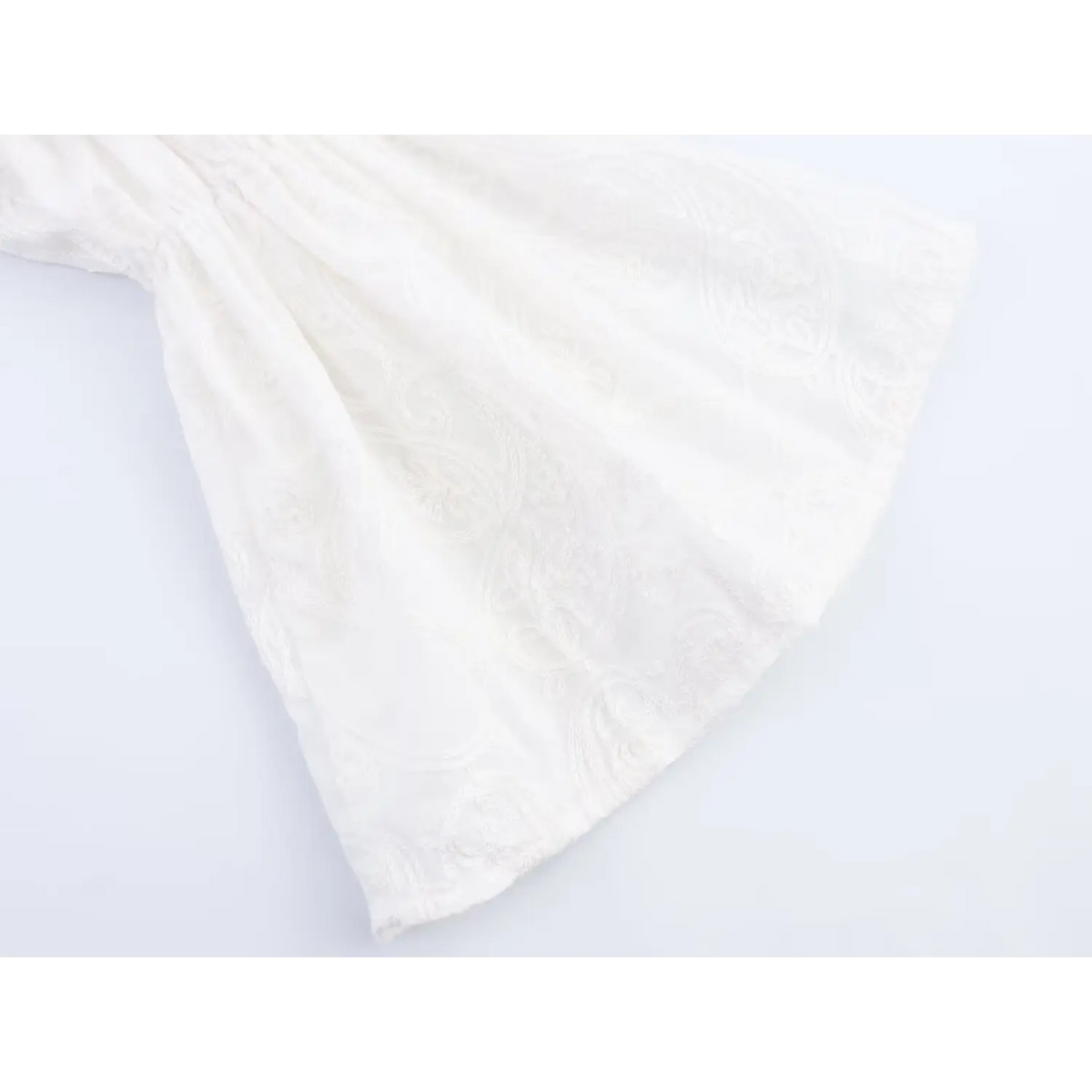 Close-up of flared bell sleeve hem, white textured jacquard fabric with embroidery