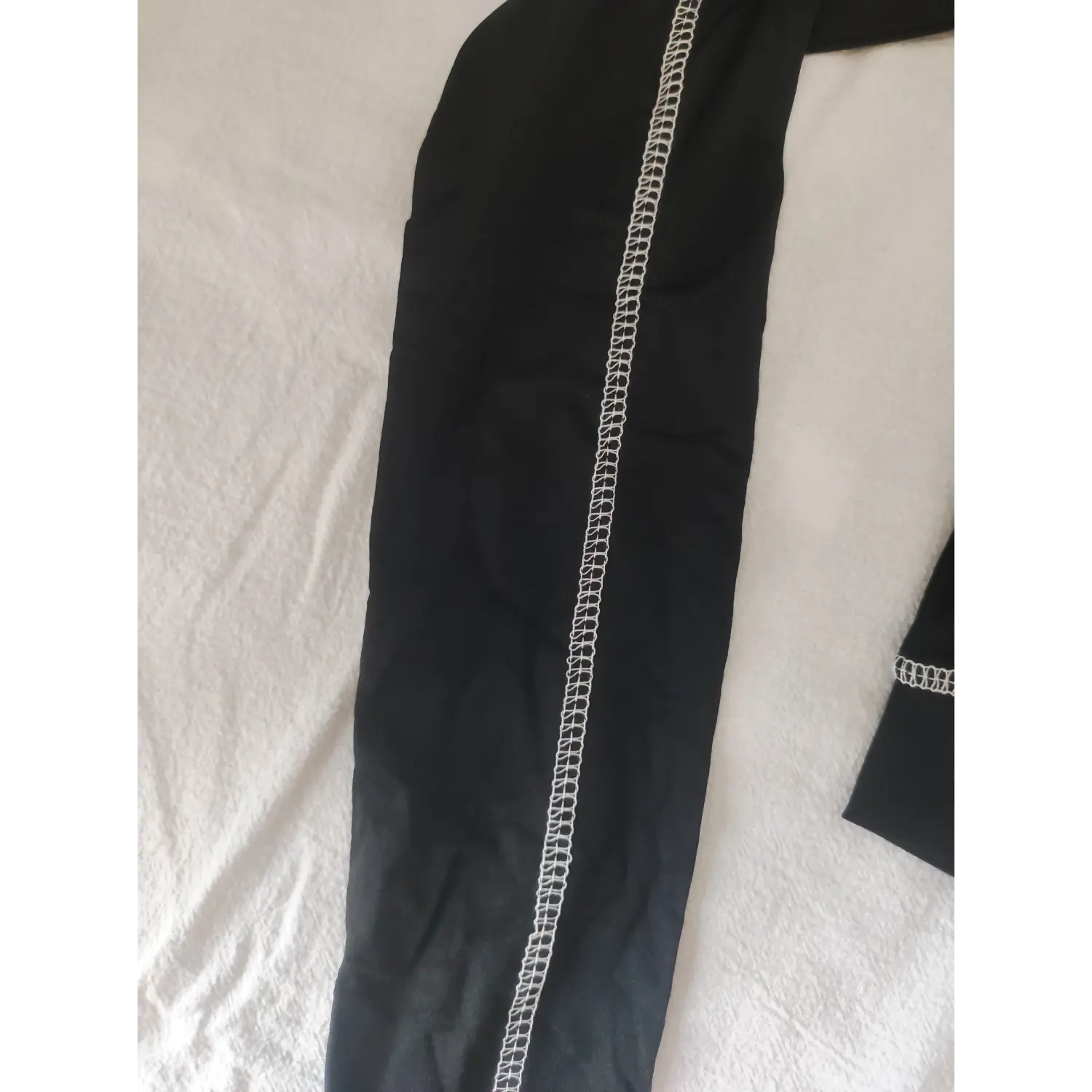 Close-up vertical white contrast stitching detail on long sleeve of black cropped athletic top