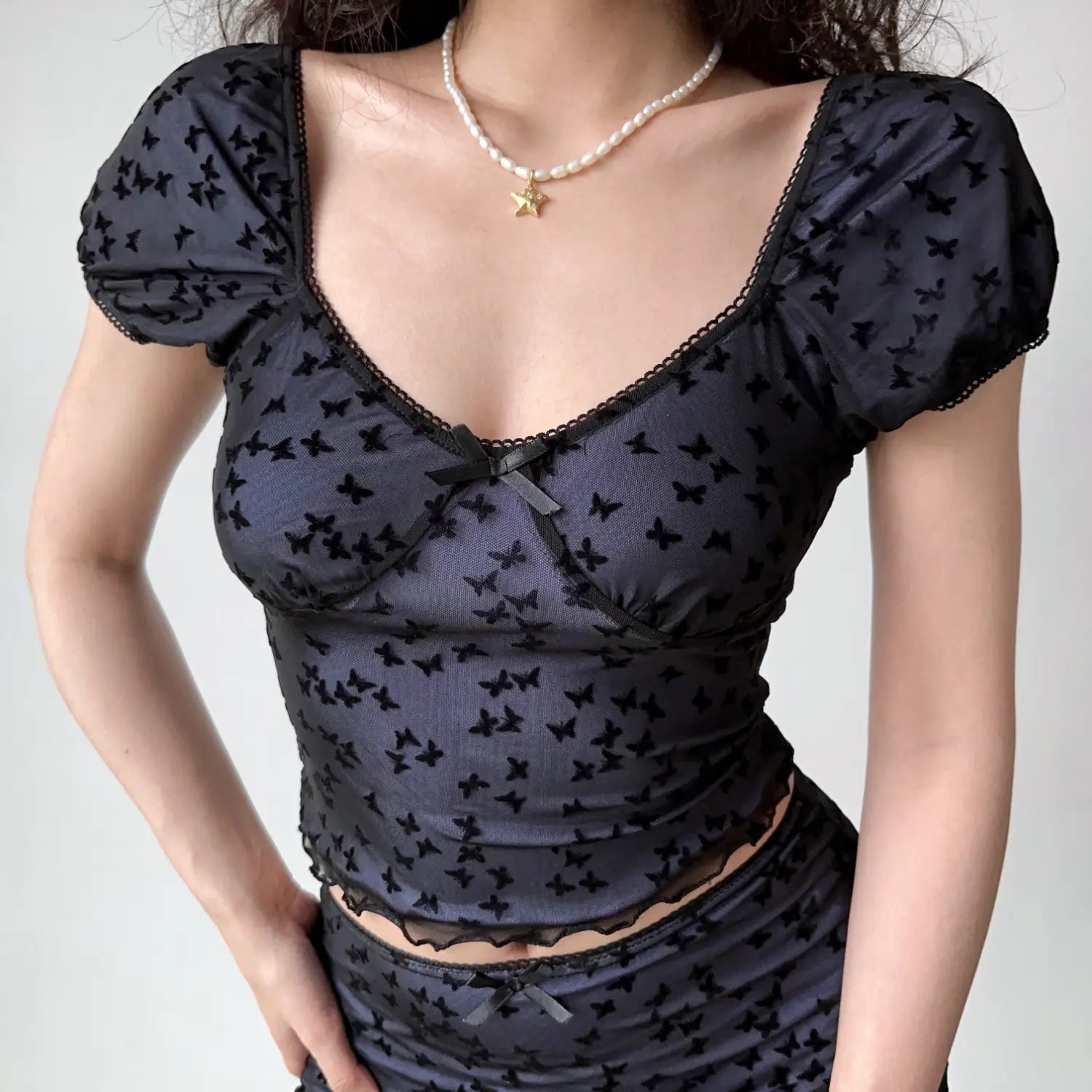 Close up black sheer mesh crop top with allover flock butterfly print, sweetheart v neck, tiny front satin bow, puff short sleeve scallop lace trim