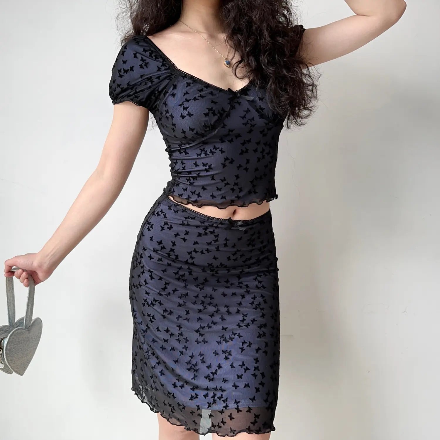 Side profile model wearing black flock butterfly mesh matching outfit, off shoulder crop top + midi length sheer skirt with ruffle hem