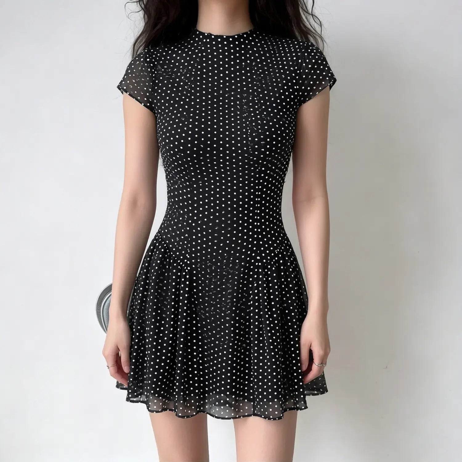Model lifestyle shot, black chiffon fitted mini dress with stand collar, cap sleeves and polka dot print