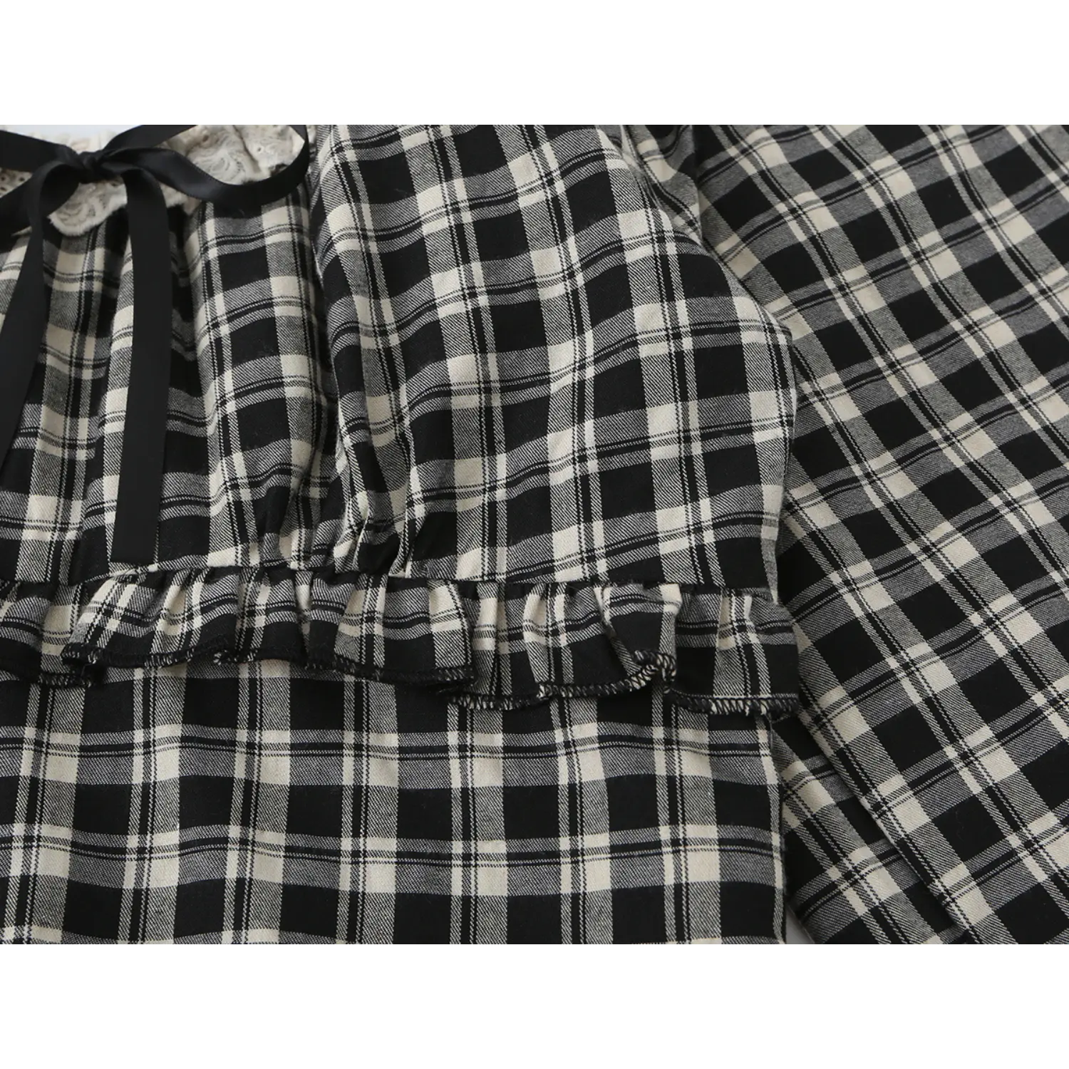 Close-up of black off-white plaid cropped blouse, front black satin ribbon bow, two-tier layered ruffle waist seam, gathered bust woven check fabric