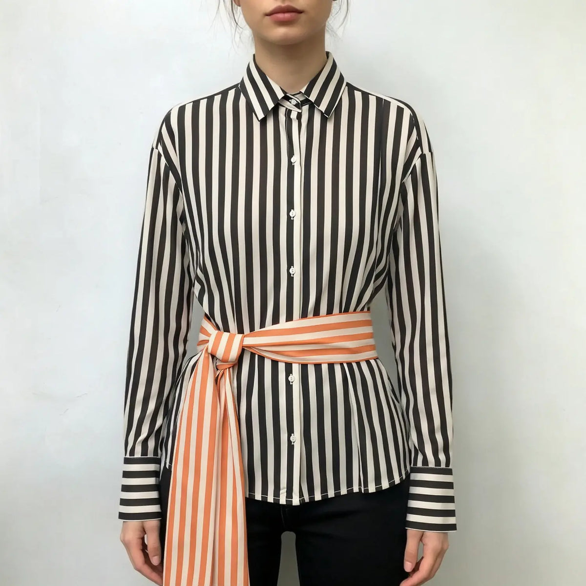 Model wearing oversized black‑cream vertical stripe collared shirt with knotted orange‑cream wrap tie belt, full front outfit view