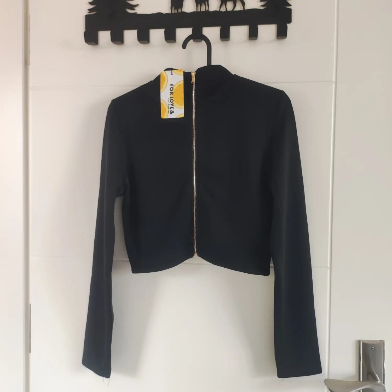 Back view black mock neck cropped top hanging on hanger with brand tag & gold zipper