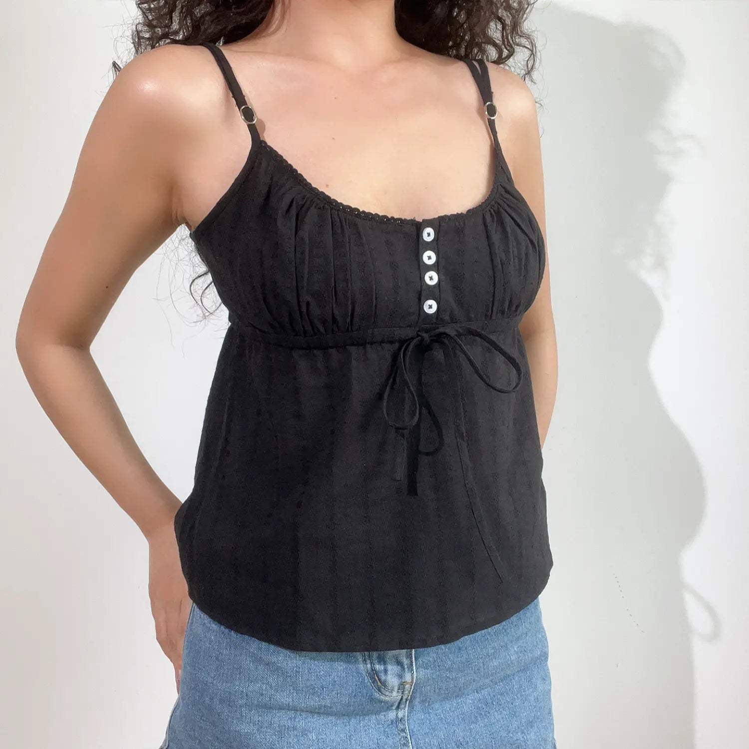 Close-up lifestyle shot of model in black textured cami top with adjustable straps and denim jeans