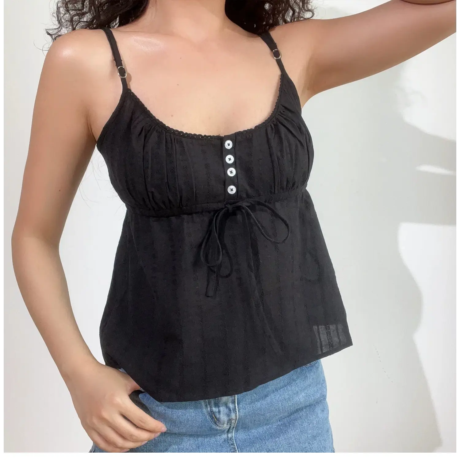 Lifestyle shot of model wearing black textured cami top with buttons and drawstring detail