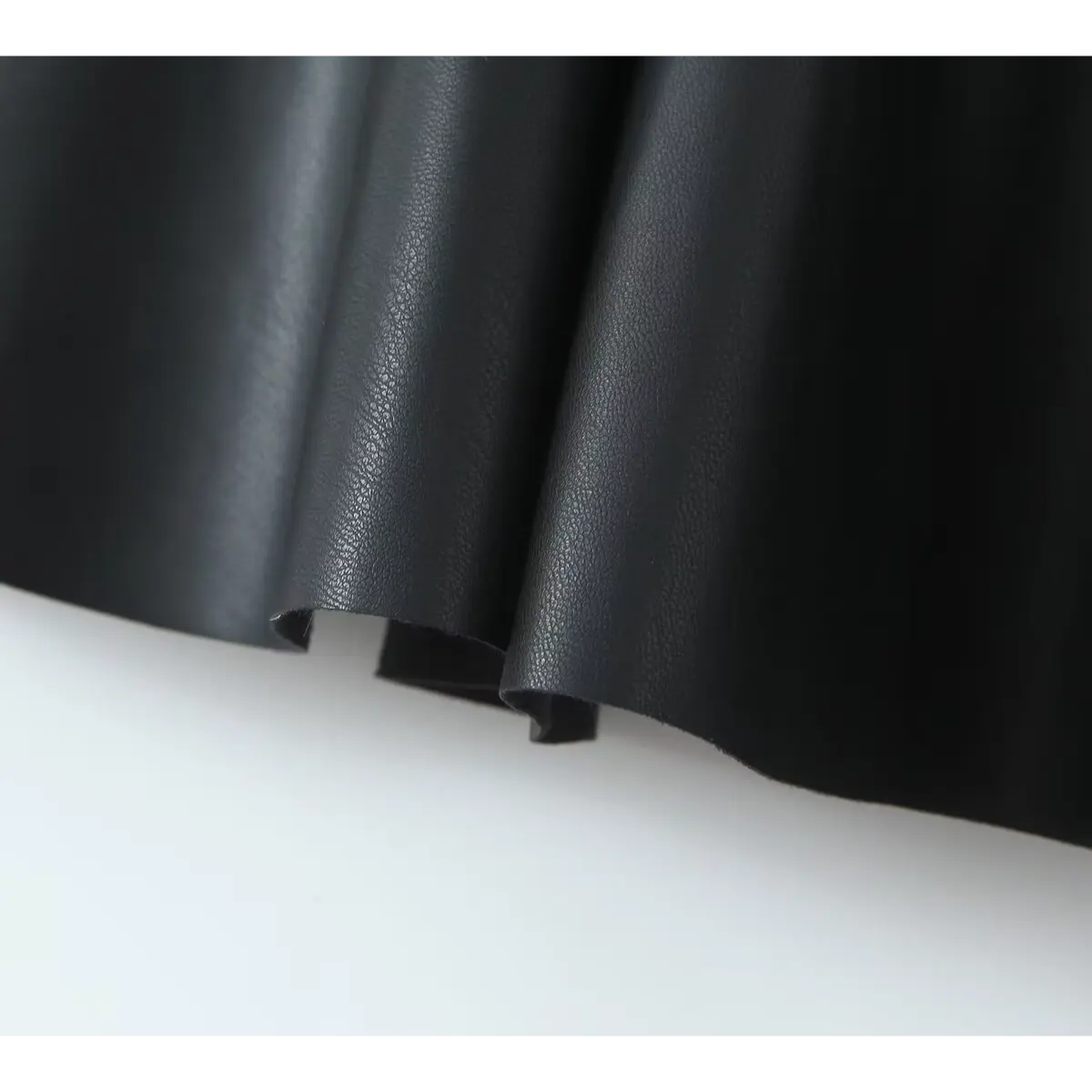 Close-up detail of the flared skirt hem and faux-leather fabric texture on a black mini dress.