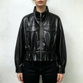 Model wearing black faux leather cropped jacket, stand collar, front zipper, flap pockets and drawstring hem