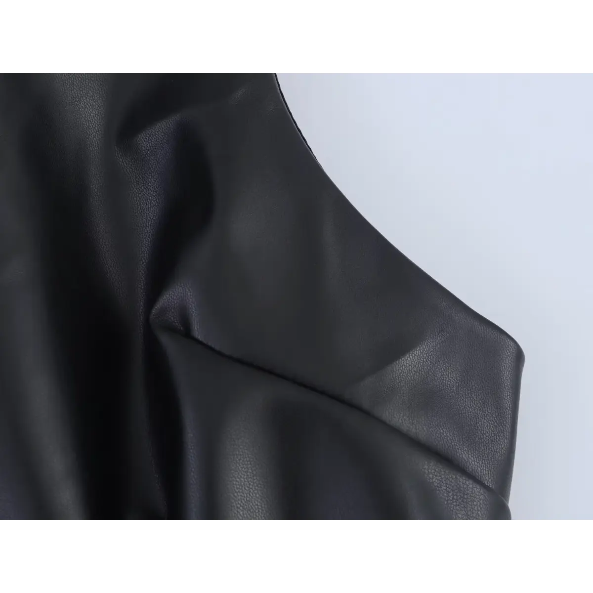 Close-up detail shot of the faux-leather fabric on a black mini dress, showing the grainy texture and natural creases.