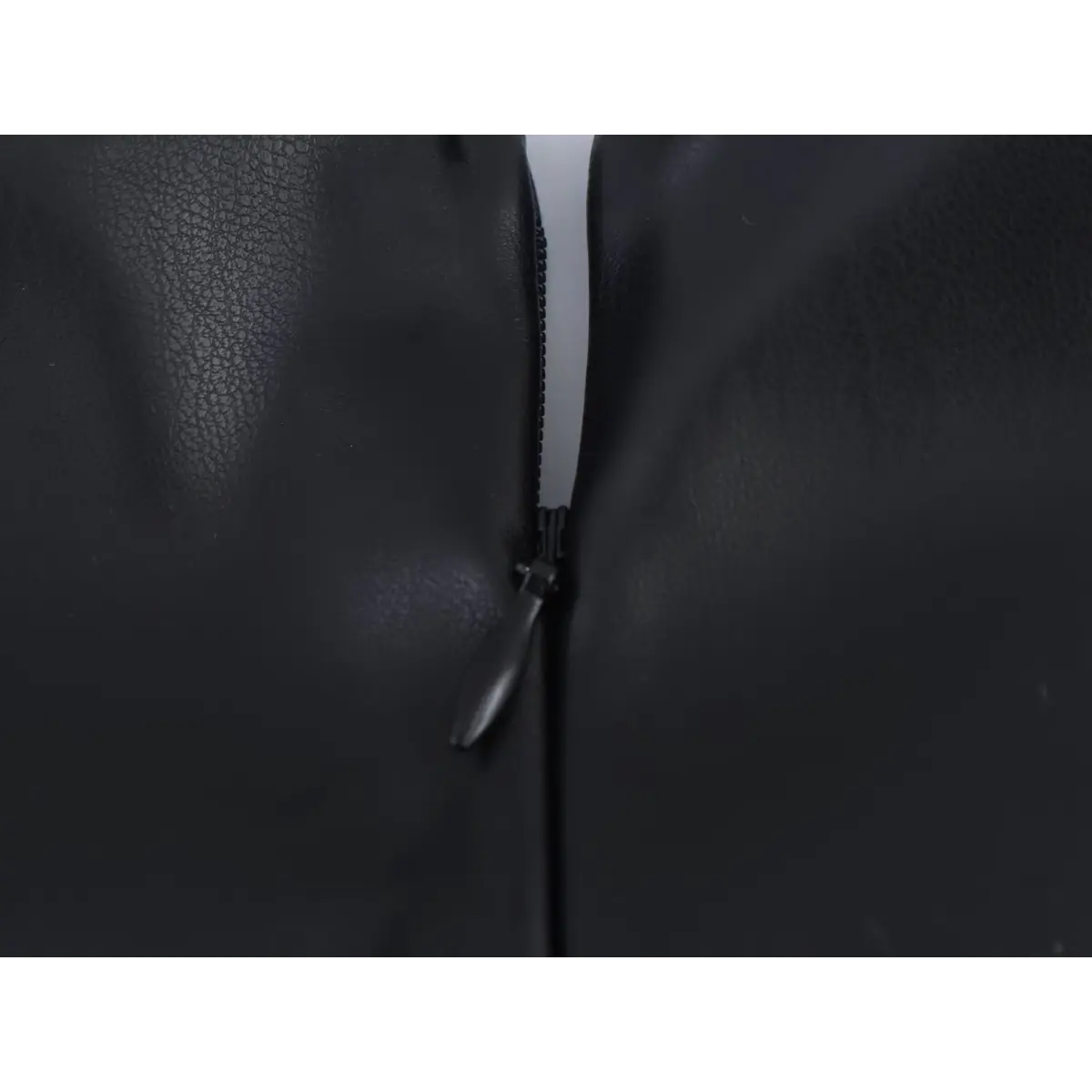Close-up detail shot of the center back zipper on a black faux-leather mini dress, showing the zipper pull and leather texture.