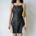 Model wearing a black faux-leather spaghetti-strap mini dress with white pleated skirt underlayer, styled with a yellow bag and green butterfly necklace, front view.