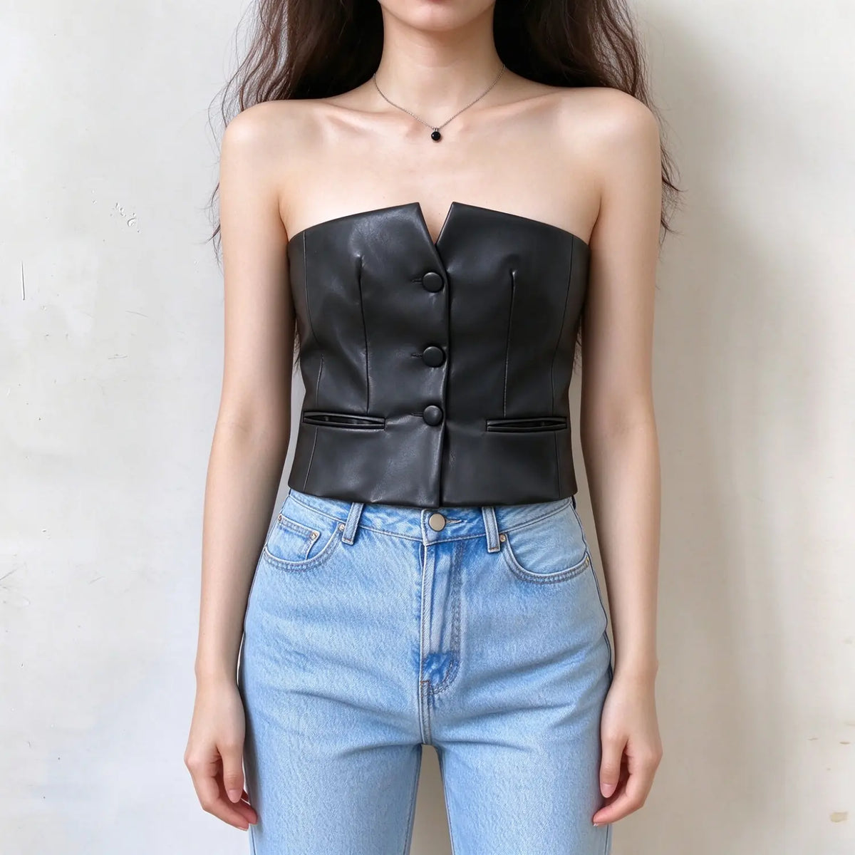 Model wearing black faux leather strapless button front crop top with jeans, front view