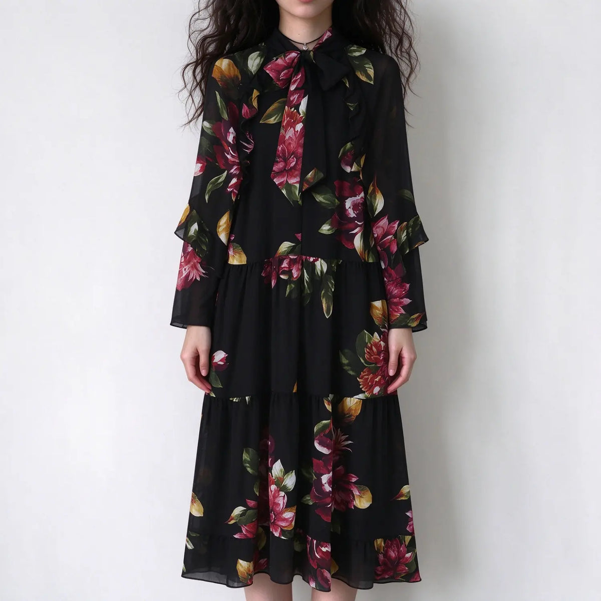 Model in black floral print chiffon maxi dress, neck bow tie, ruffle tiered long sleeves, flowy tiered long skirt, front view