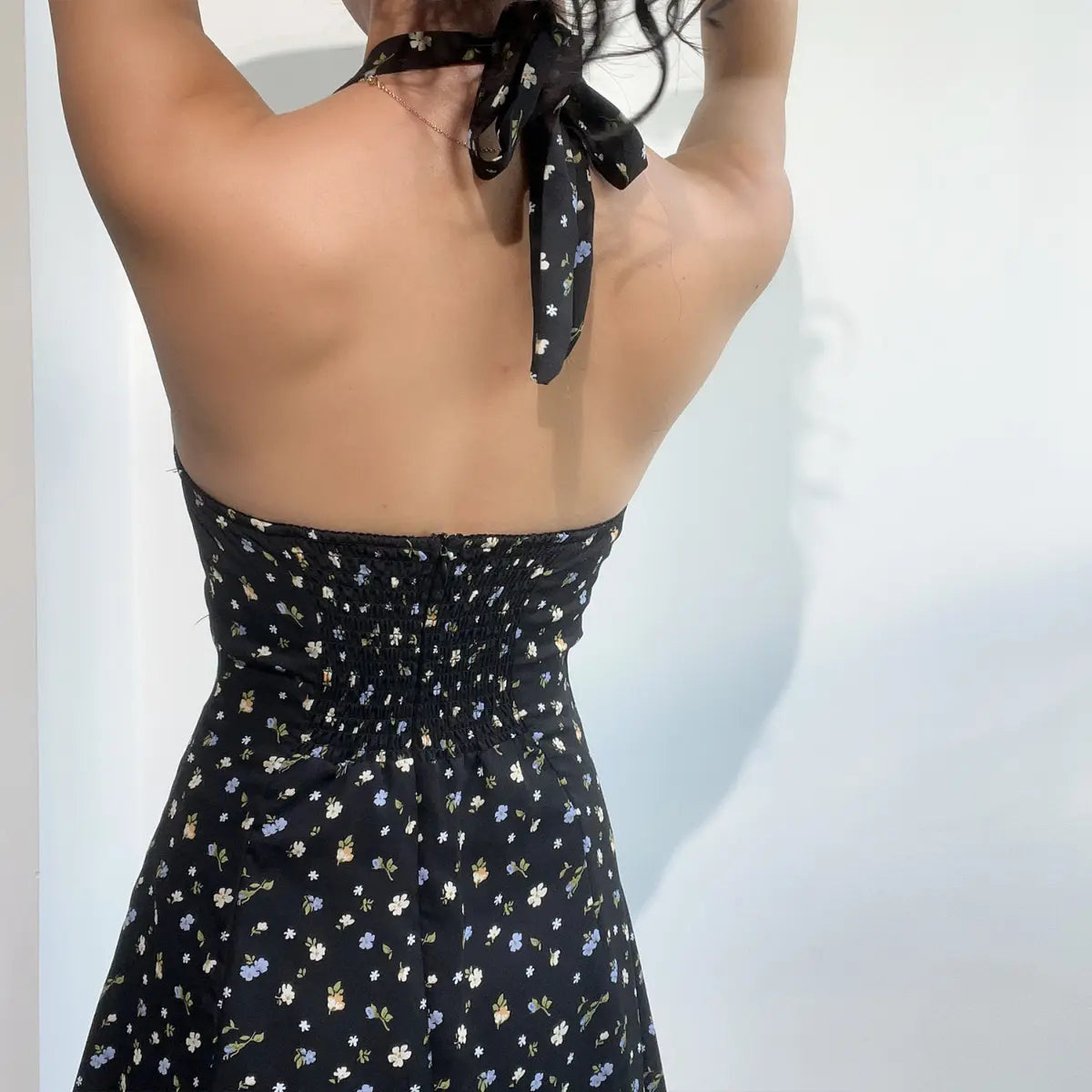  Close-up of the back view of a black floral halter dress, showing the tie neck and smocked back panel