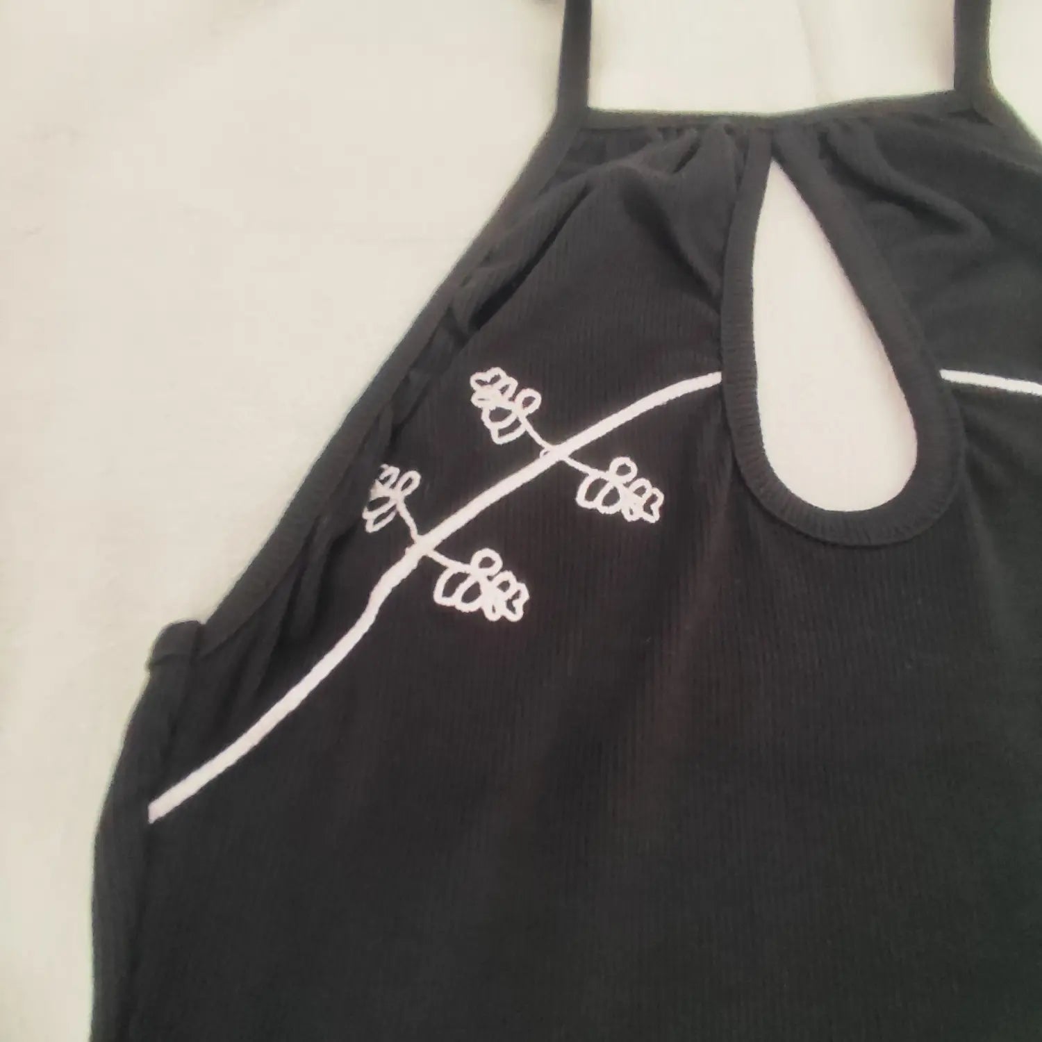 Close‑up shot halter keyhole neck and white floral embroidery detail on black ribbed mini dress