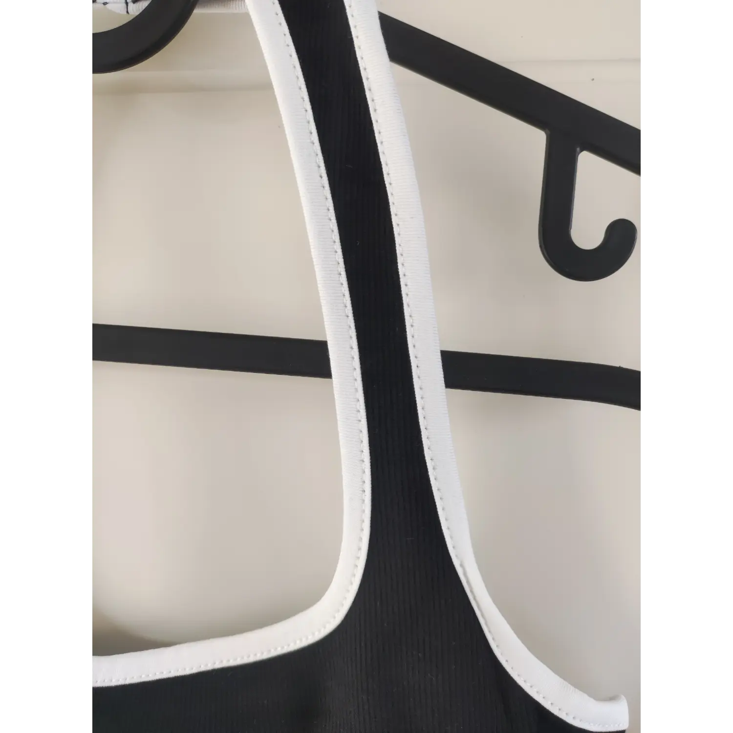 Close‑up detail of halter strap stitching and white contrast piping on black ribbed dress