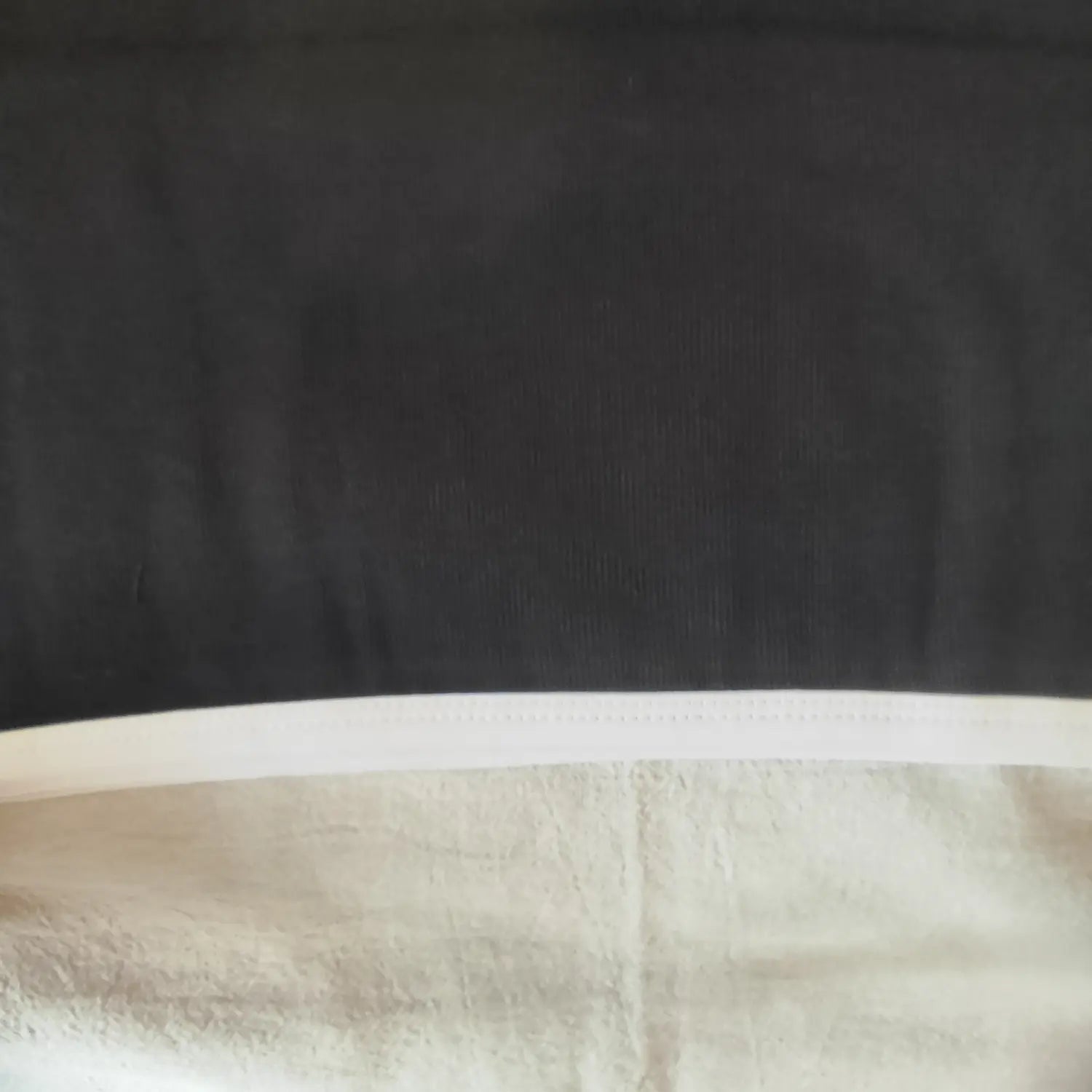 Close‑up of bottom hem white contrast piping stitching on black ribbed mini dress