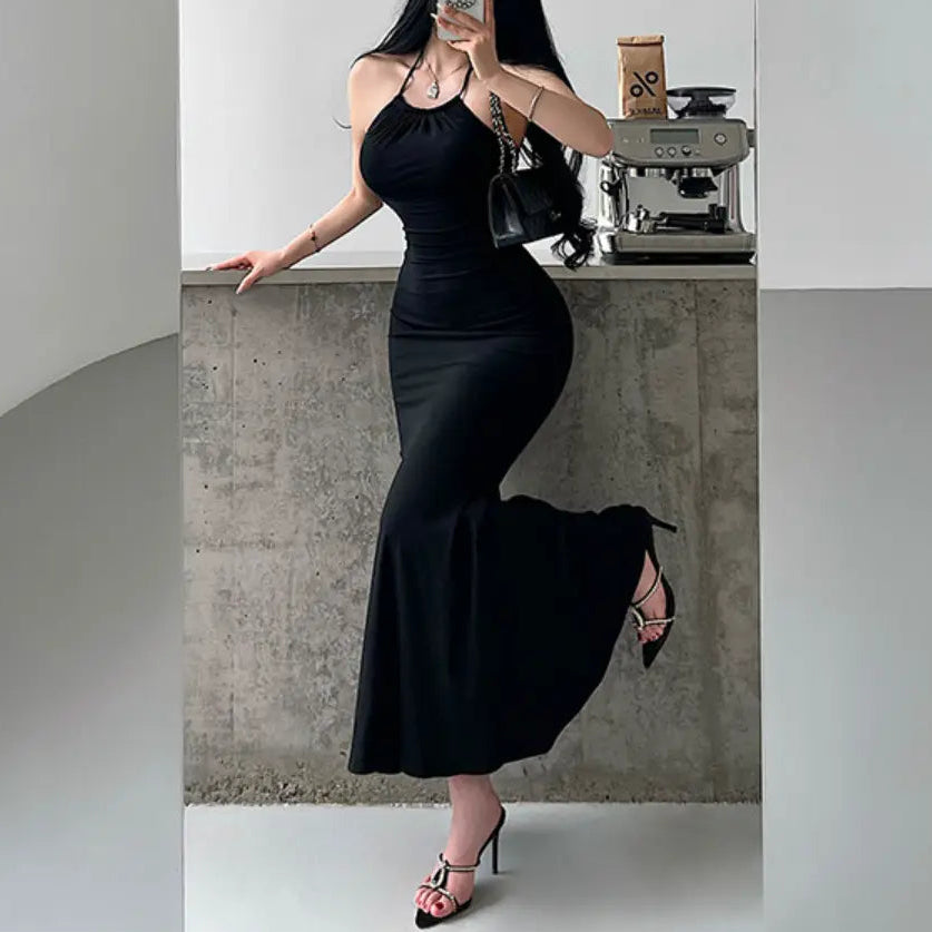 A woman wearing a black halter-neck mermaid maxi dress with ruched waist and bodycon fit, styled with black accessories.