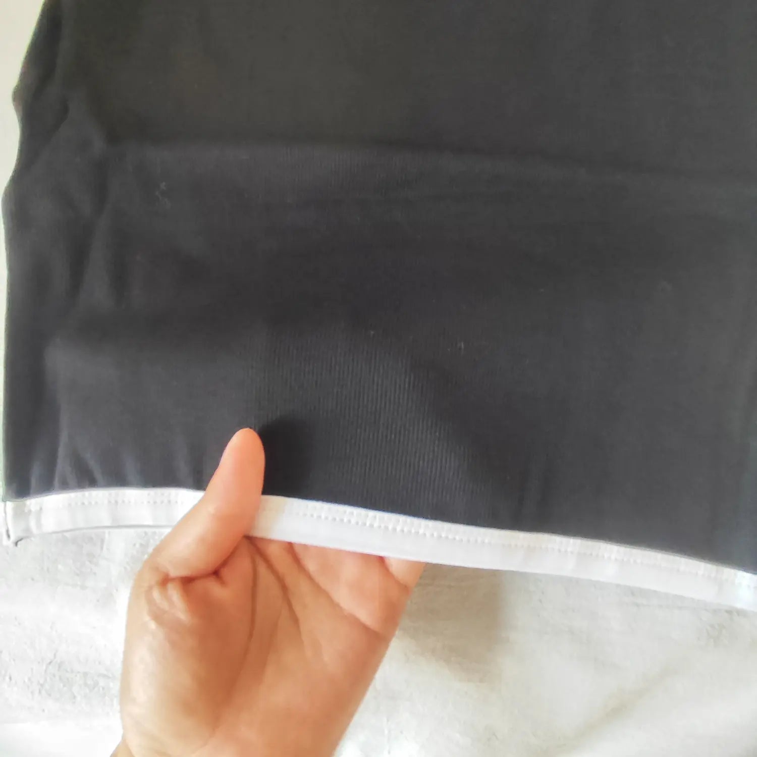 Close‑up hand holding bottom hem with white contrast piping of black ribbed halter mini dress