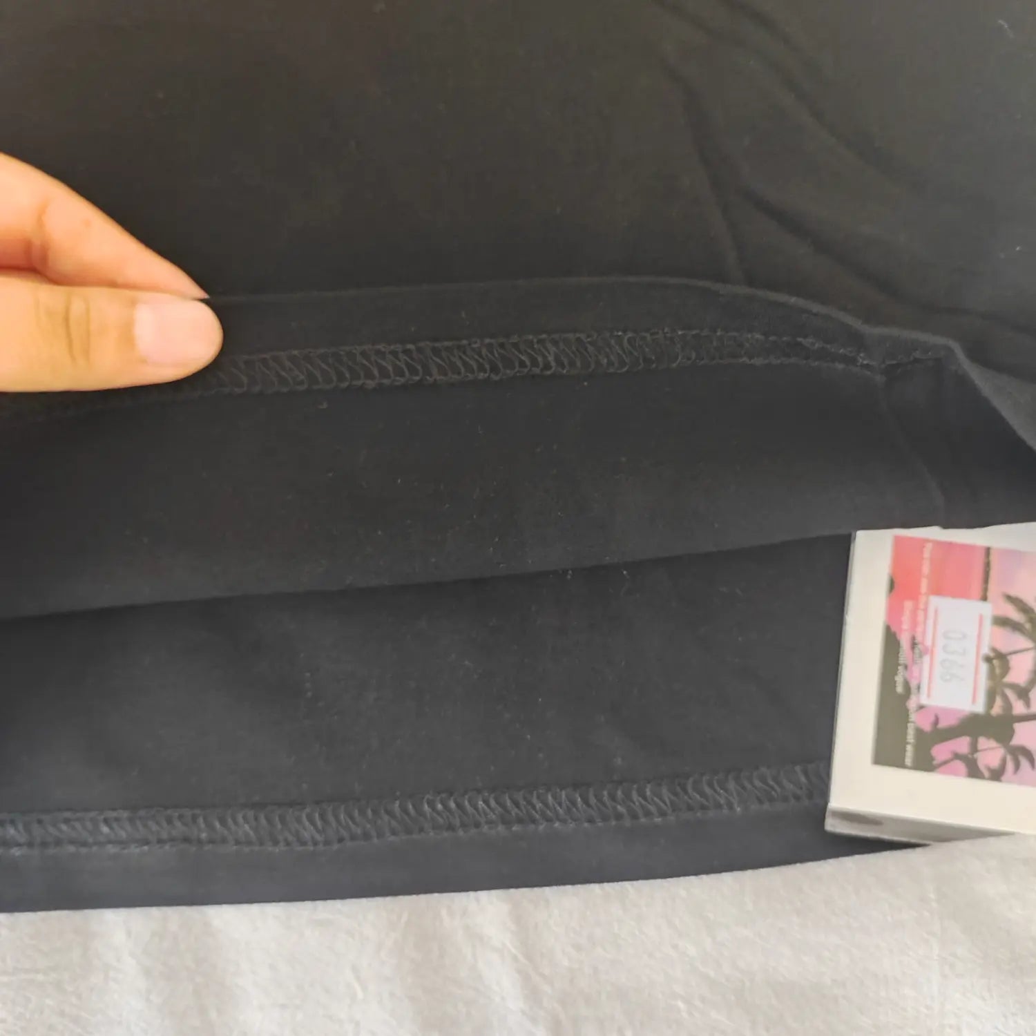 Close‑up bottom hem stitching and paper tag detail black graphic print halter tank top