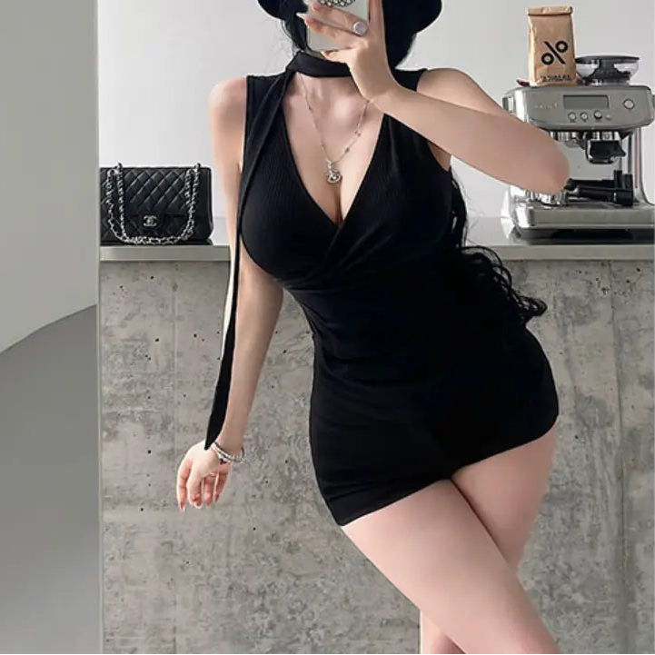  A woman wearing a black ribbed halter wrap top with a tie detail, styled with black shorts and a hat, taking a mirror selfie.