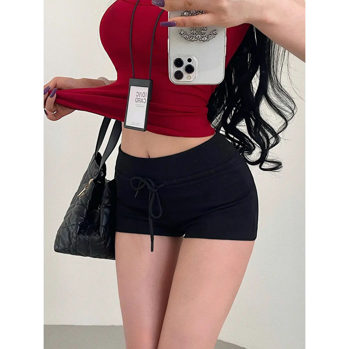 Close-up of a woman wearing black high-waisted drawstring shorts with a red cropped top, styled with a quilted bag.
