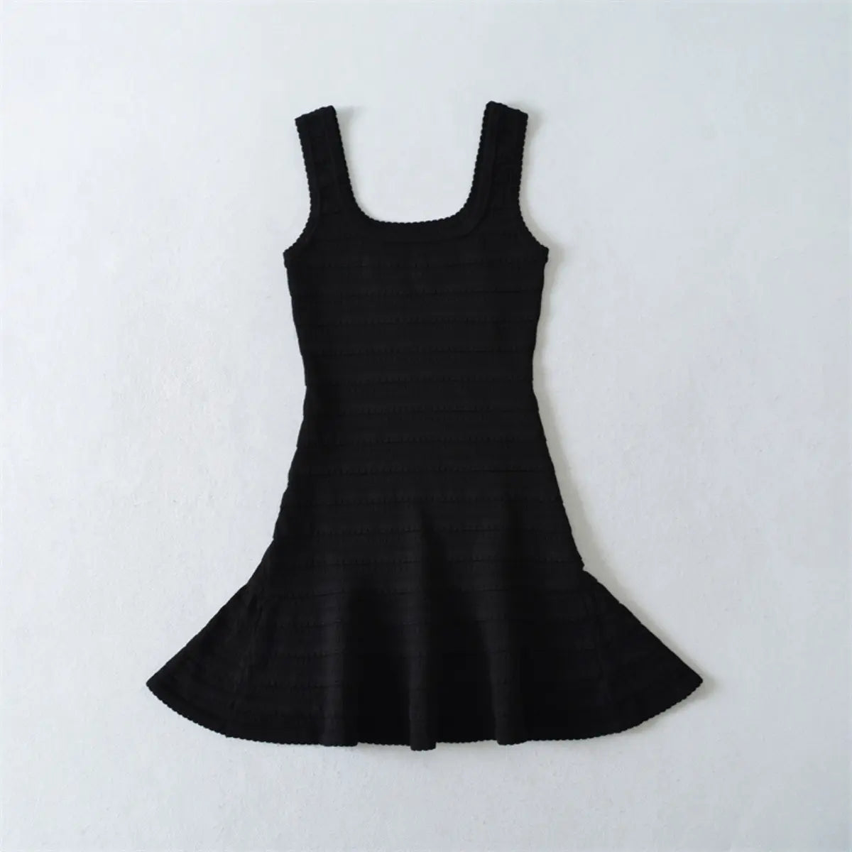Flat lay view of a black knit mini dress, showing the full silhouette with square neckline, fitted bodice, and flared skirt.