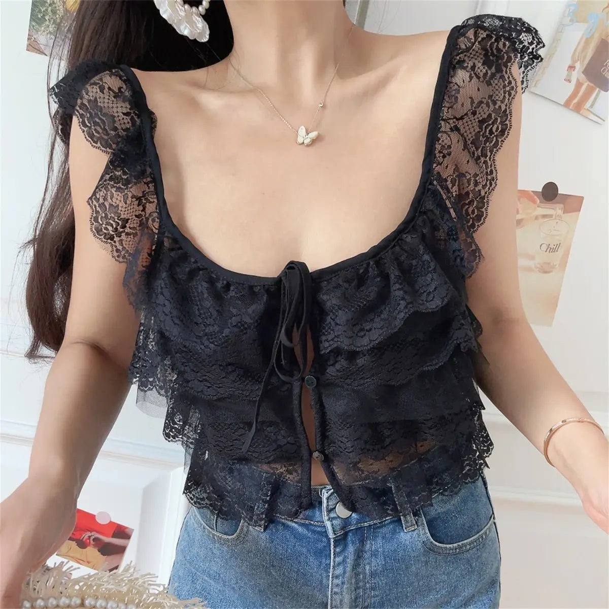  Front view of a woman wearing a black layered lace camisole with a front tie and buttons, paired with jeans.