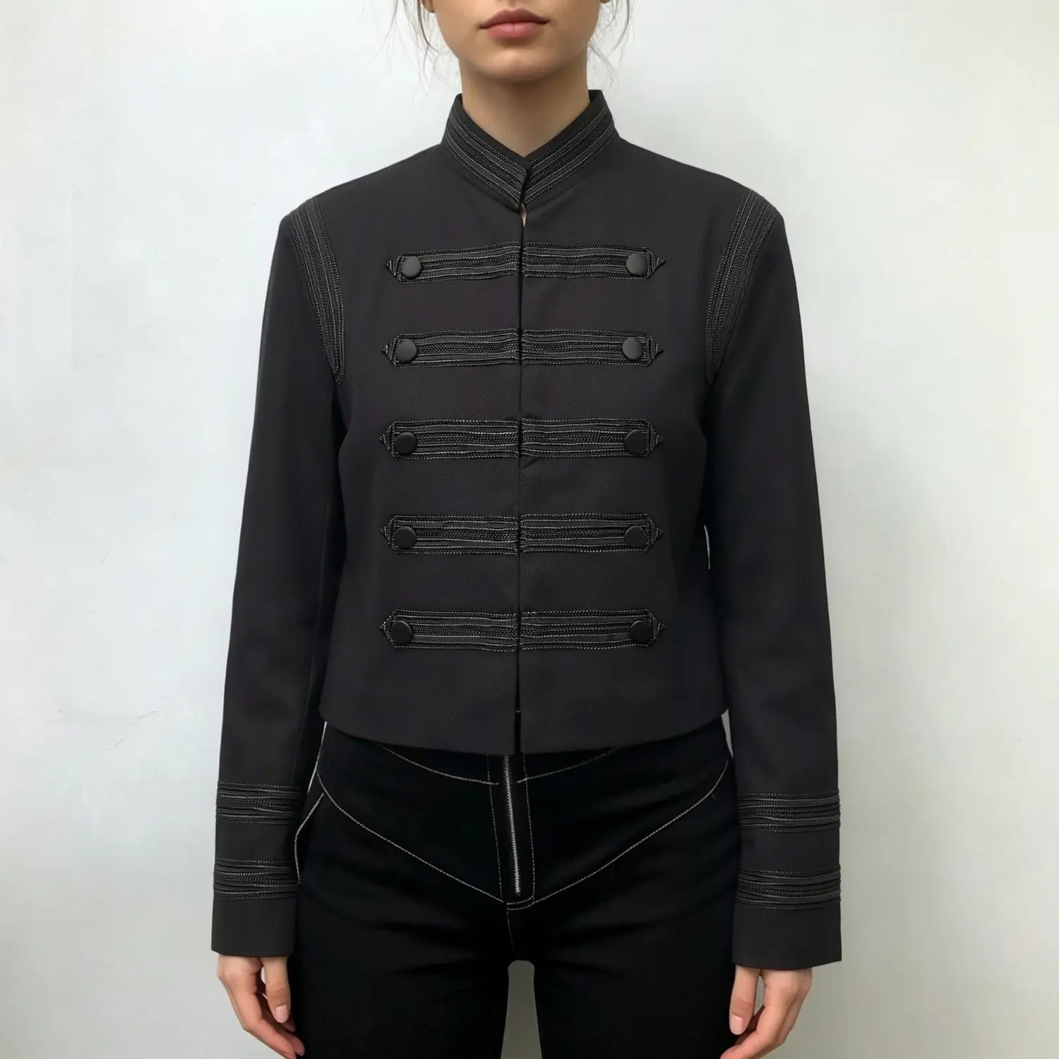 Model wearing black military inspired cropped jacket, stand collar, decorative button detailing, paired with black pants, front full torso shot