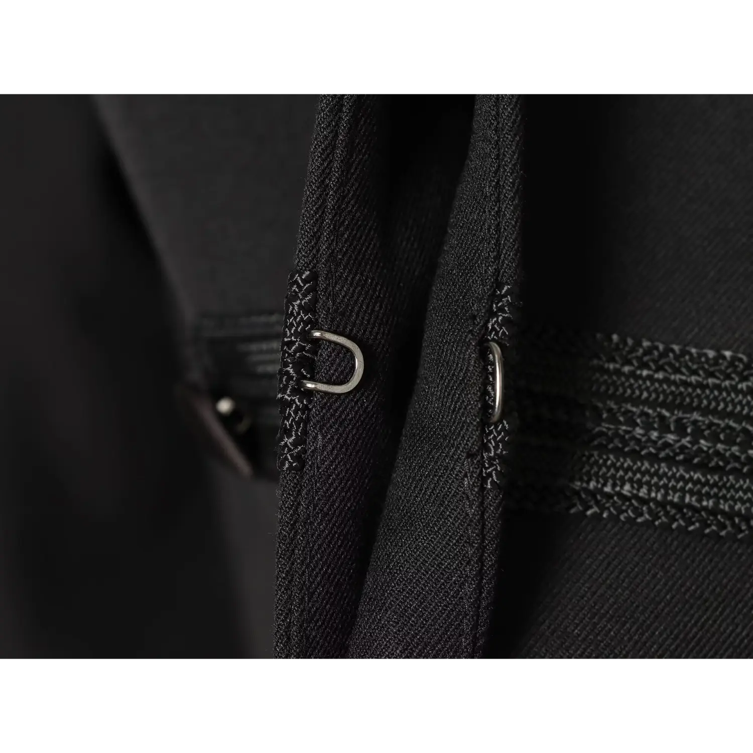 Macro close‑up of metal hook clasp fastener inside placket of black military cropped jacket