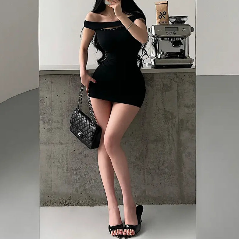 A woman taking a mirror selfie while wearing a black ribbed off-shoulder mini dress with stud details, styled with bunny ears, a Chanel bag, and platform sandals.