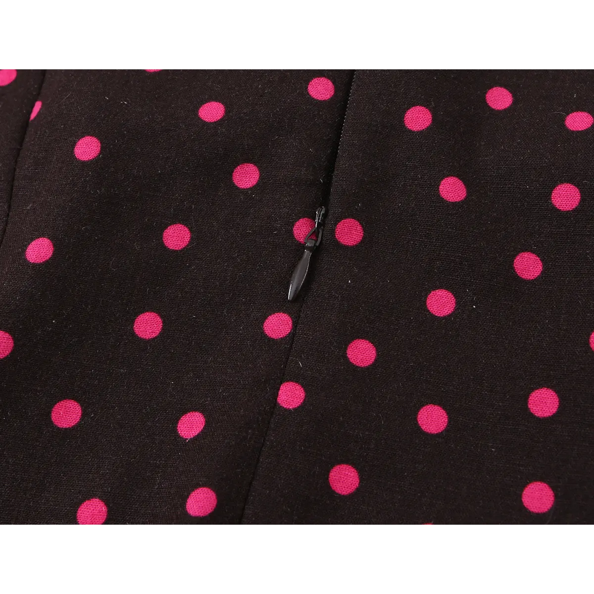 Close-up of the dress's hidden zipper, showing the black pull tab against the polka dot fabric.