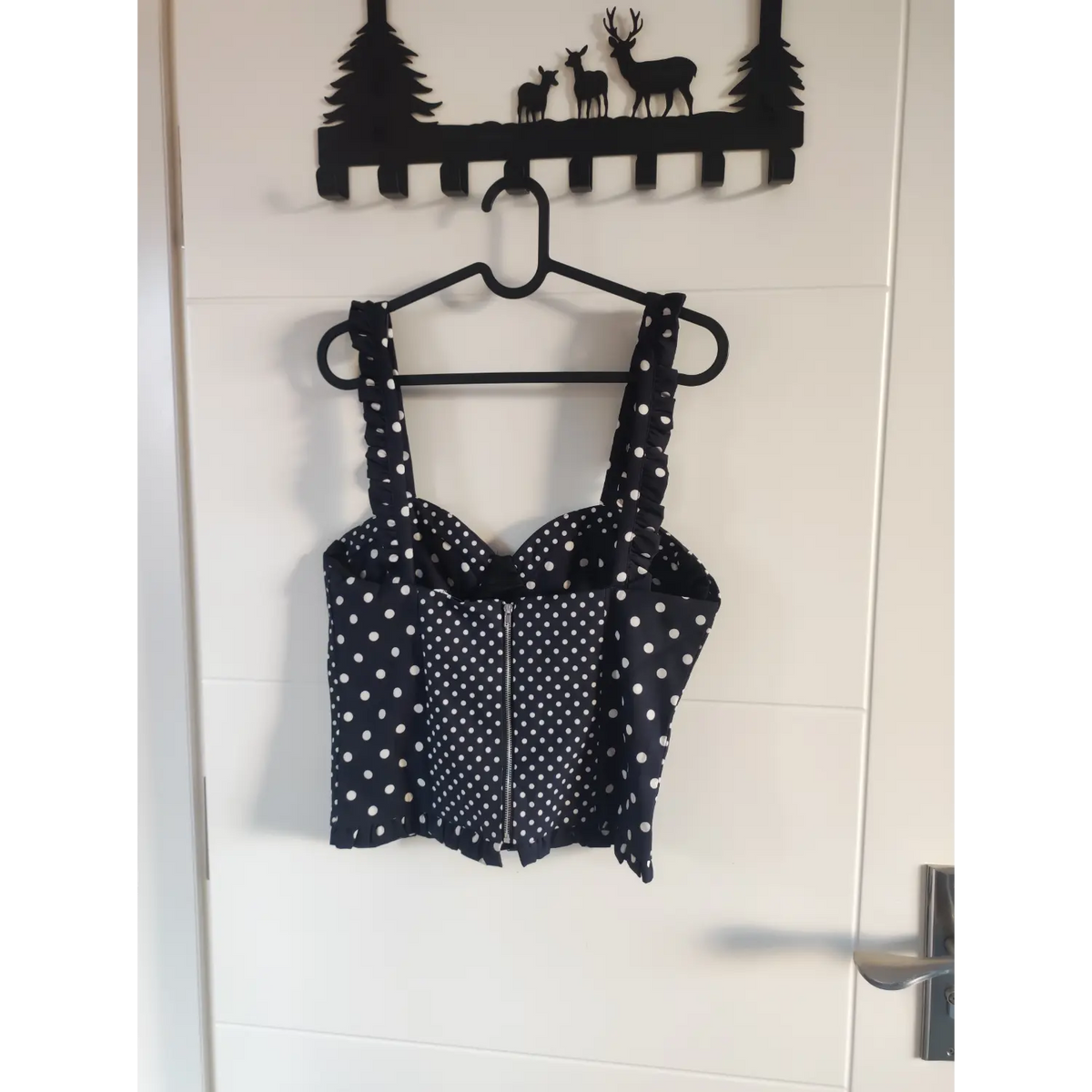Back view of black polka dot corset crop top with center zipper hanging on hanger