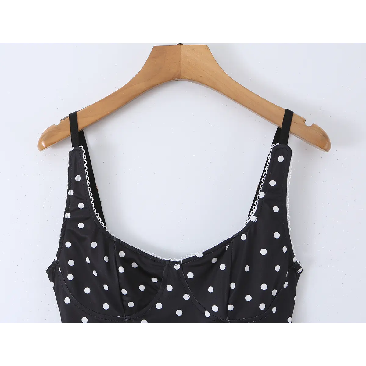 Black polka dot cami top hanging on wooden hanger, showing silhouette and straps