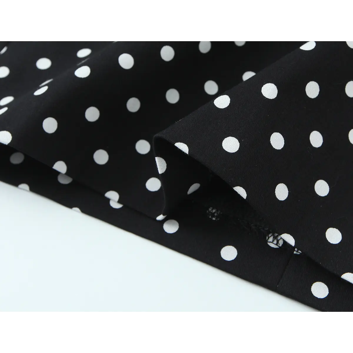 Close-up of the dress's fabric, showing the drape, polka dot pattern, and seam construction at the hem