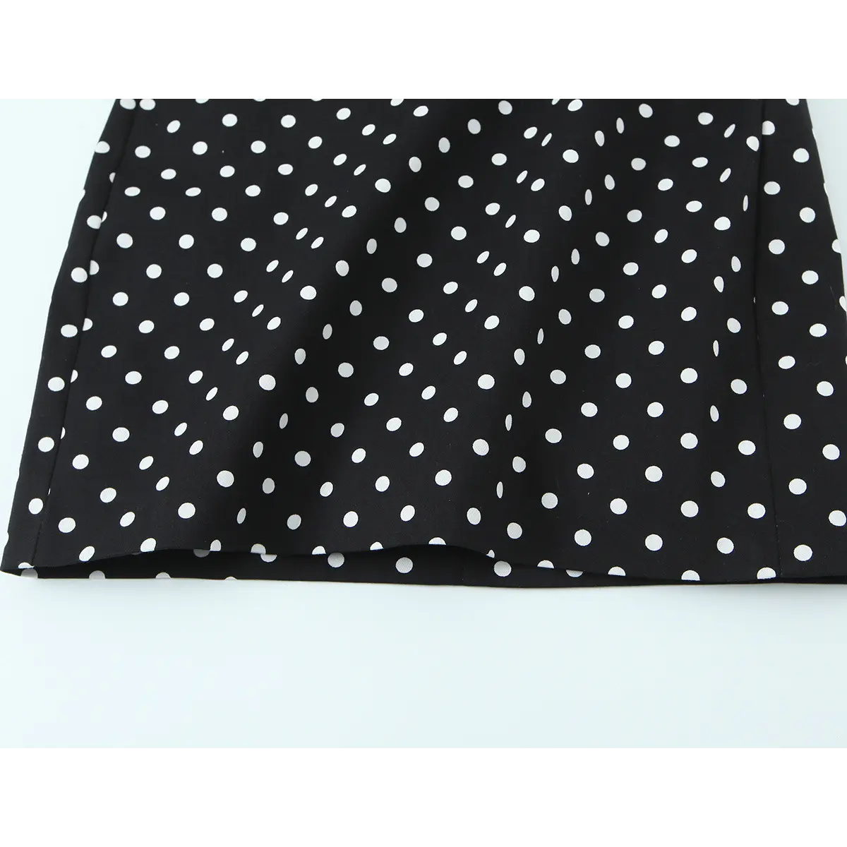  Close-up of the dress's hem, displaying the black fabric with evenly spaced white polka dots and clean edge stitching.