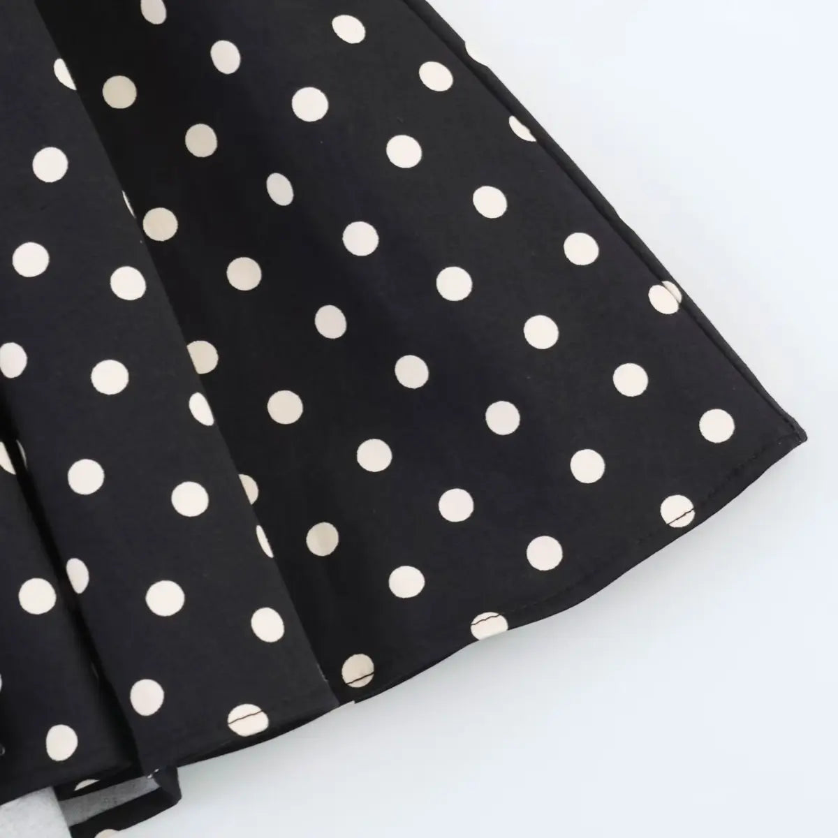 Close-up of the flared skirt hem on black polka dot dress, showing finished edge and pleated design.