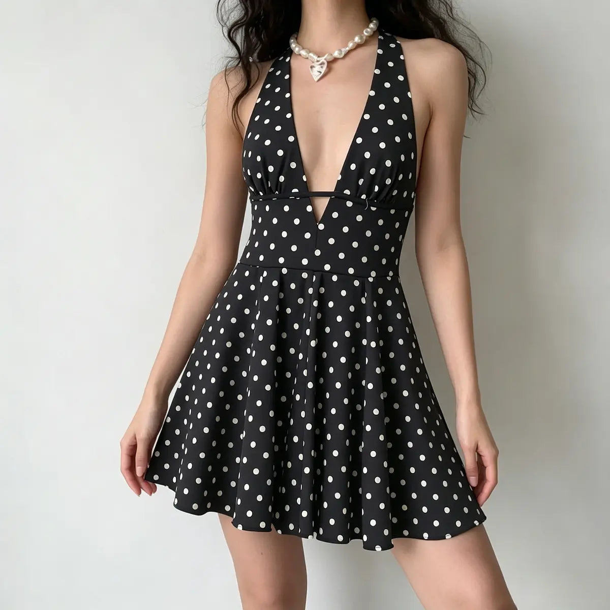 Full front view of model in black polka dot halter mini dress, emphasizing the deep V-neck and flared A-line skirt.