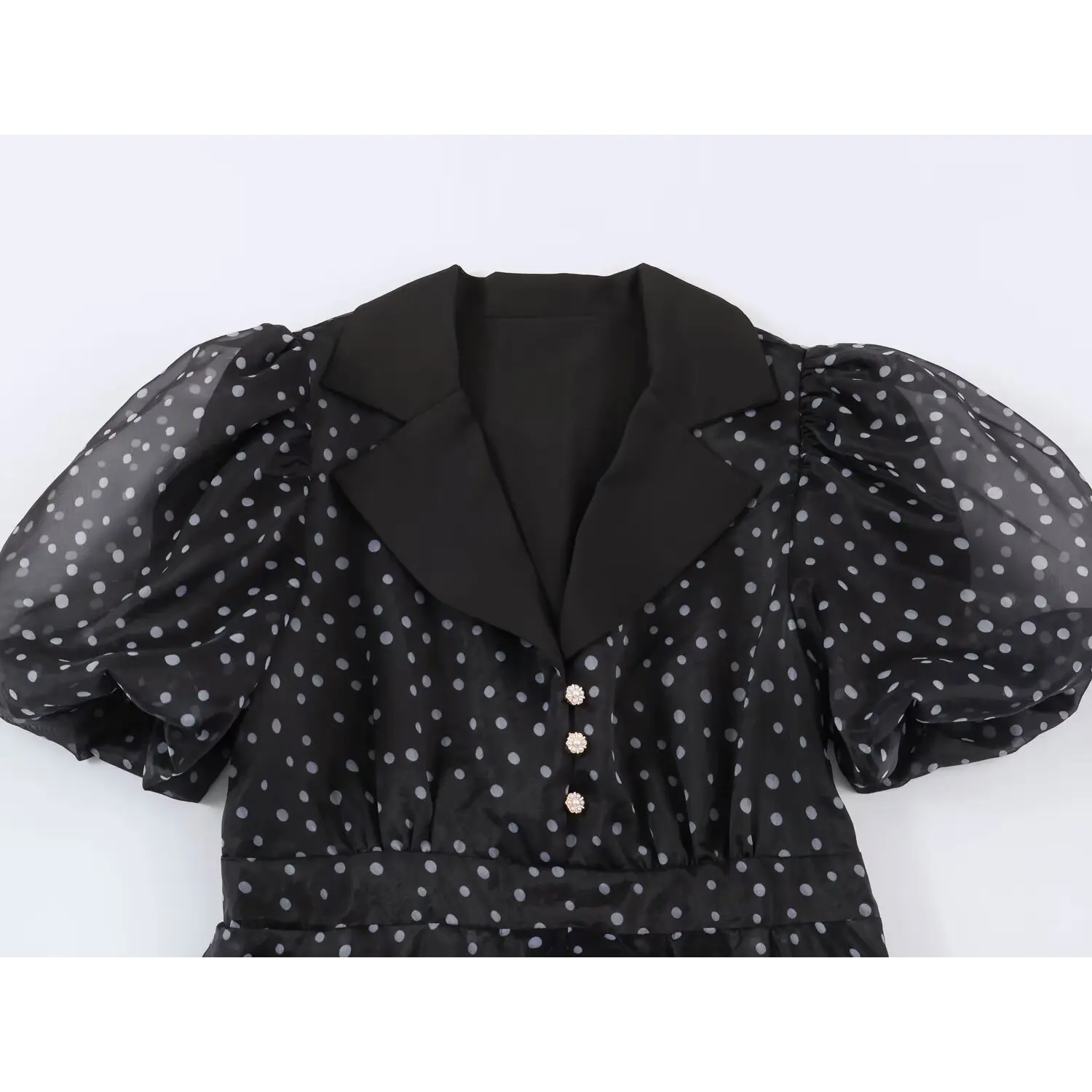 Flat‑lay close‑up of lapel collar and decorative pearl buttons on black polka dot maxi dress