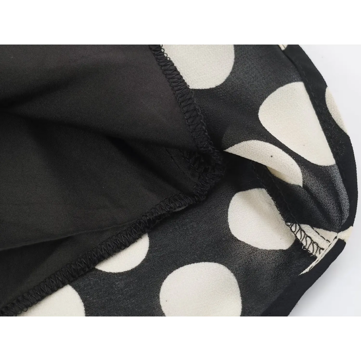 Close-up of hem stitching, inner lining and semi-sheer outer fabric of black polka dot maxi dress