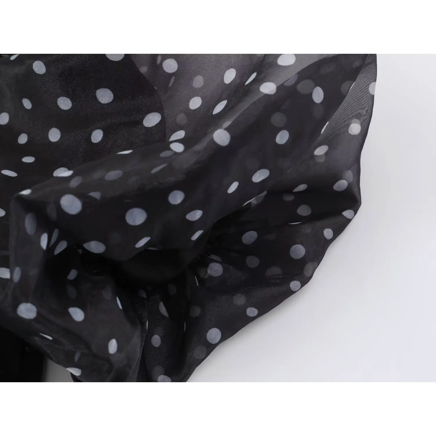 Close‑up folded sheer organza fabric of black polka dot maxi dress, showing fabric translucency