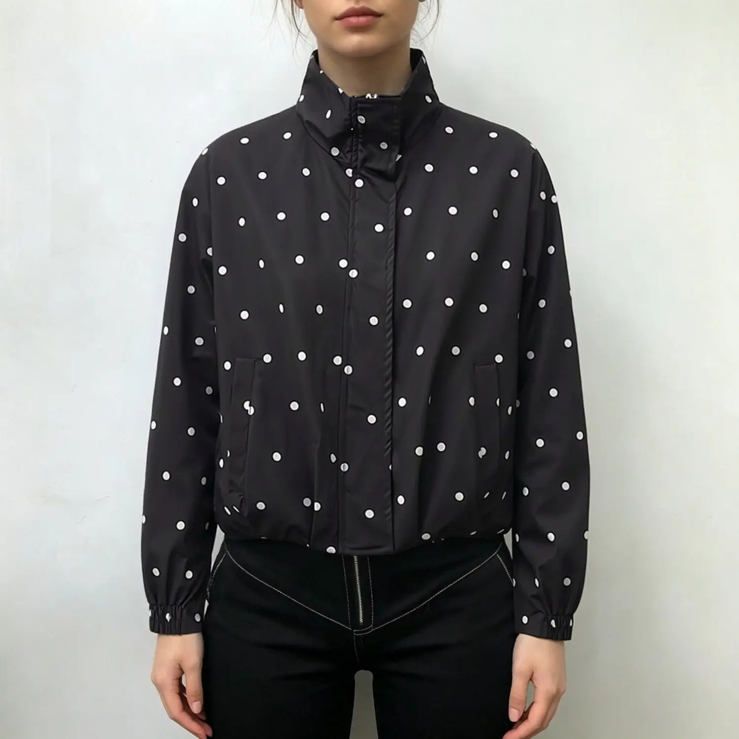 Model wearing black cropped polka dot windbreaker jacket, stand collar, relaxed fit, paired with black pants