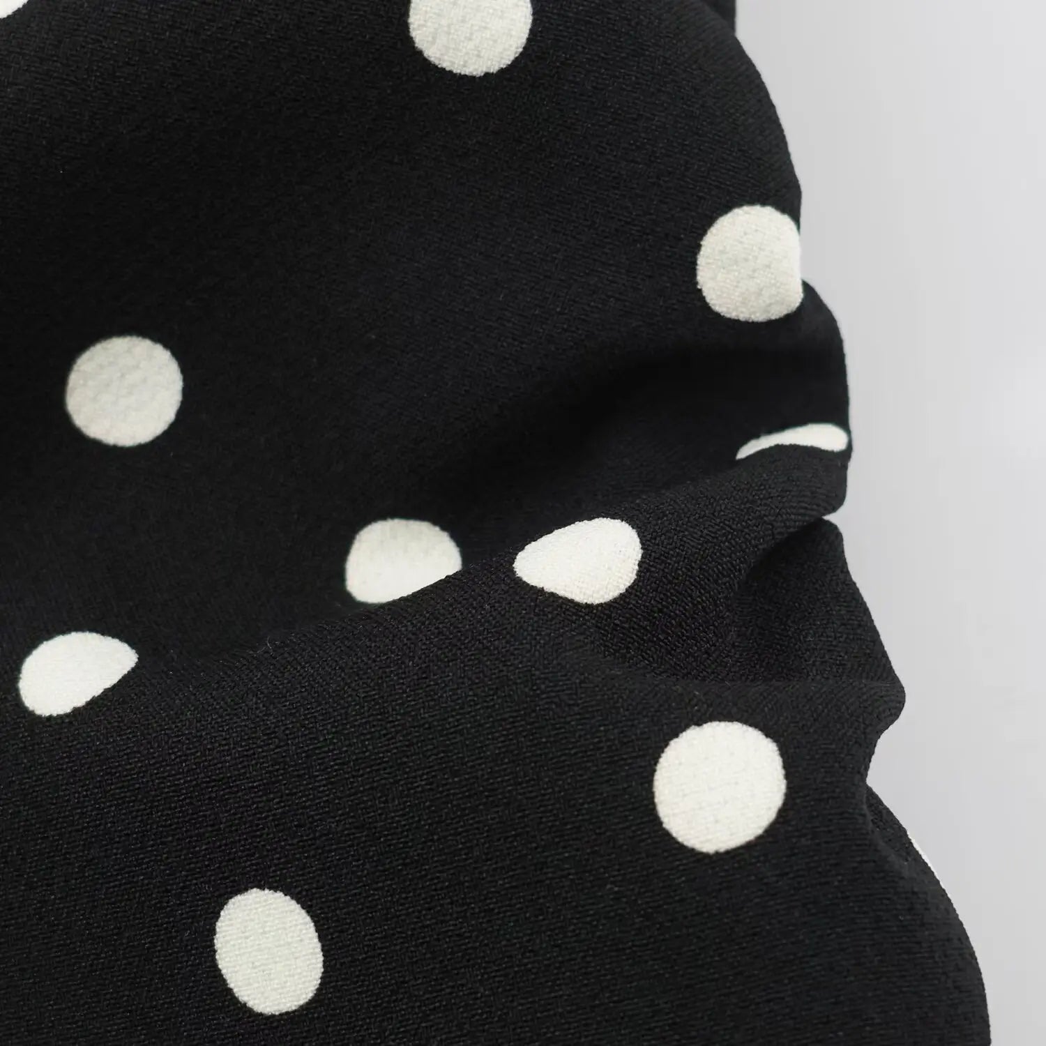 Wrinkle close‑up of black woven fabric with white polka dot pattern
