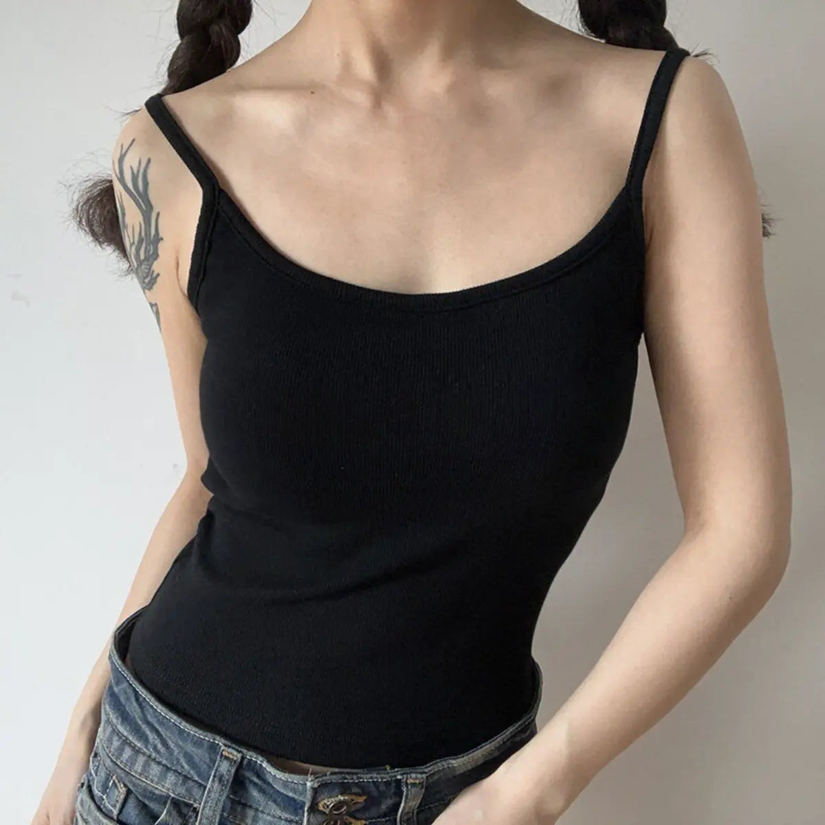 Lifestyle shot of form-fitting black ribbed camisole with thin straps, tucked into jeans
