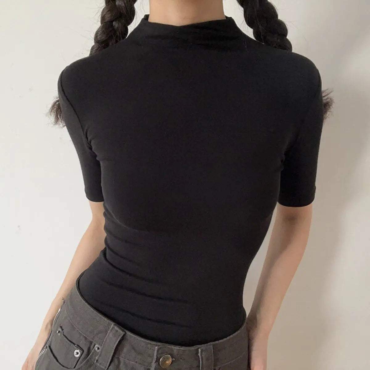 Lifestyle shot of form-fitting black ribbed half-turtleneck short-sleeve top, tucked into jeans