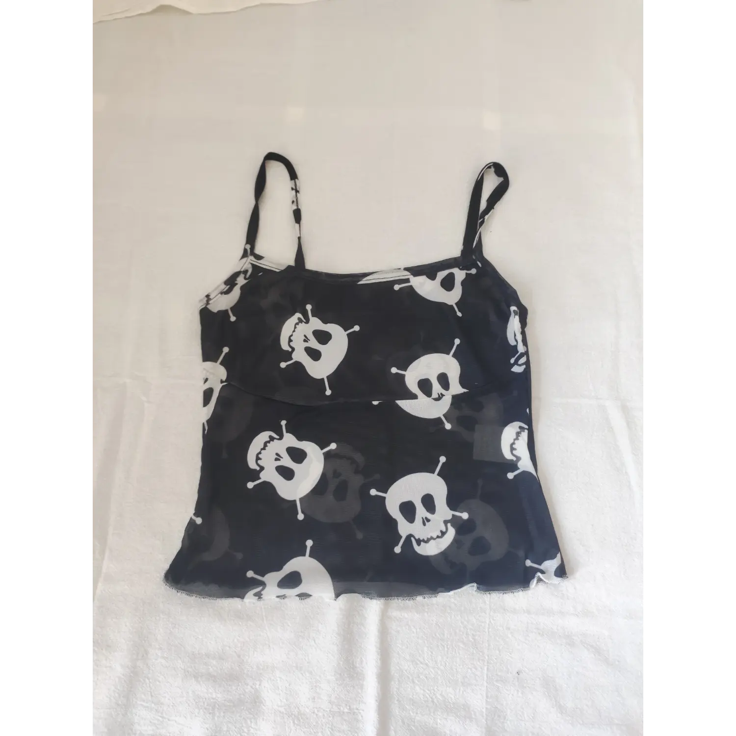 Flat lay front view black sheer mesh cami top with white cartoon skull print, spaghetti straps, lettuce hem goth crop tank top