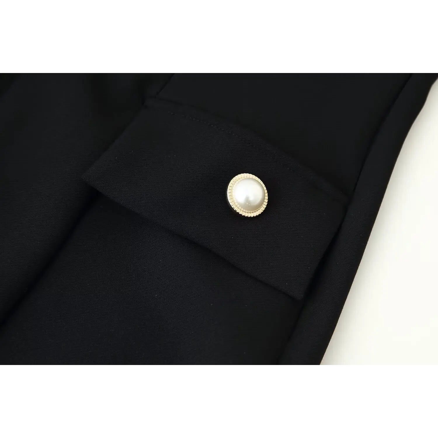 Close‑up decorative pearl gold button on faux pocket of black mini dress