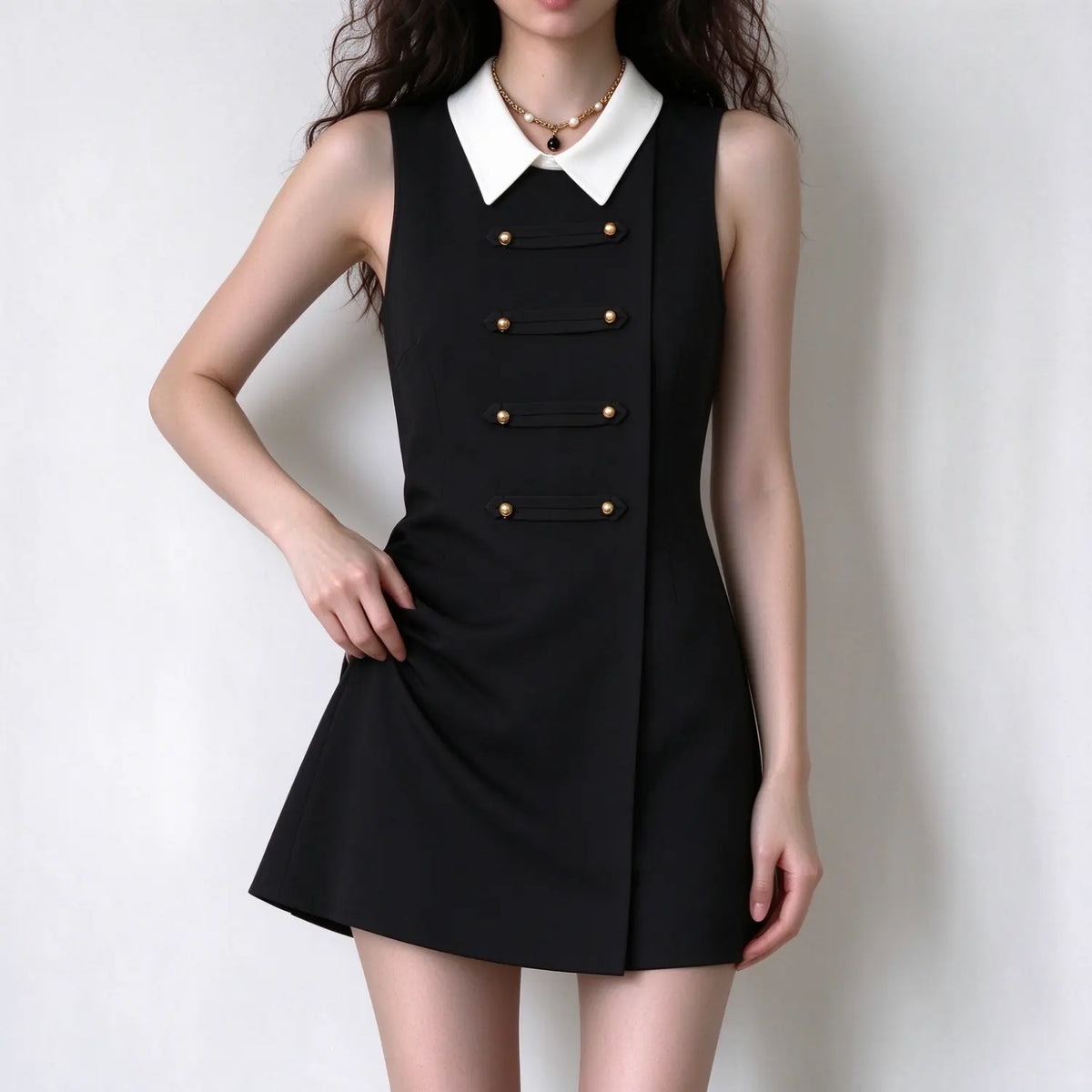 Female model wearing black sleeveless mini dress with white collar, one hand gently lifts skirt fabric to show material drape