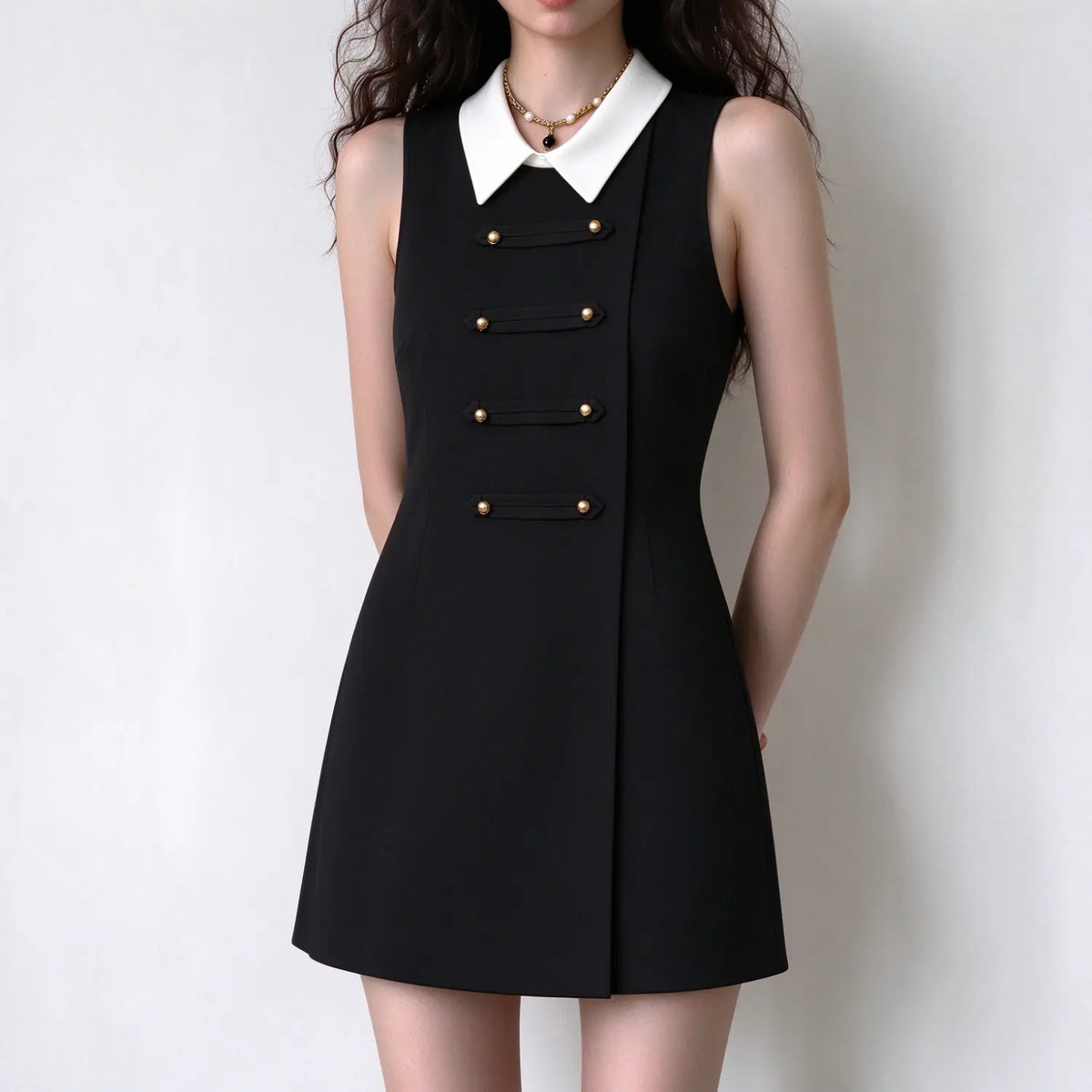 Female model in black collared sleeveless mini dress, gold double button strips on front, hands placed behind back, show neat silhouette