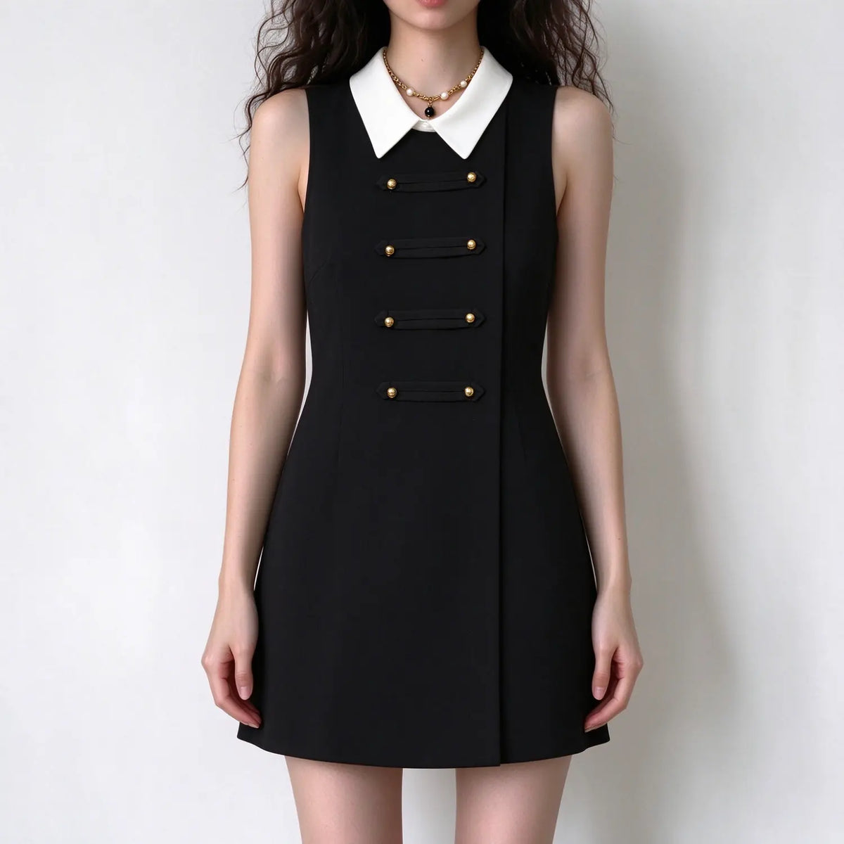 Female model stands straight, black sleeveless mini dress with contrast white collar and gold decorative buttons, clean front view display